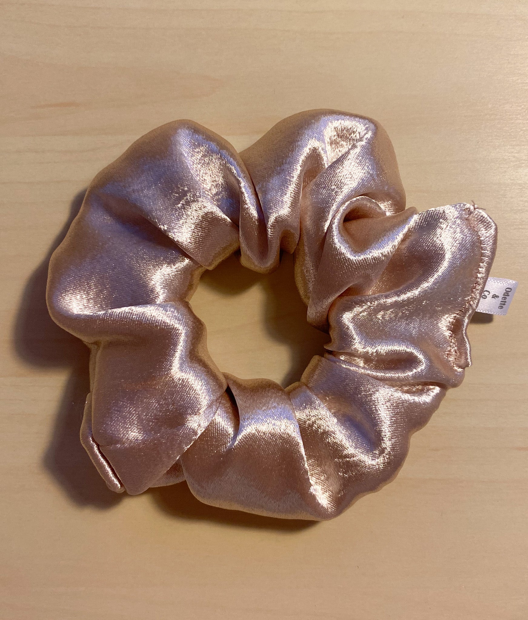 close up flat lay image of pink champagne satin scrunchie 