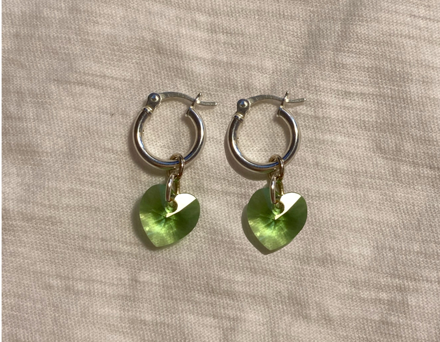 flat lay image of green crystal heart earrings with sterling silver hoops 