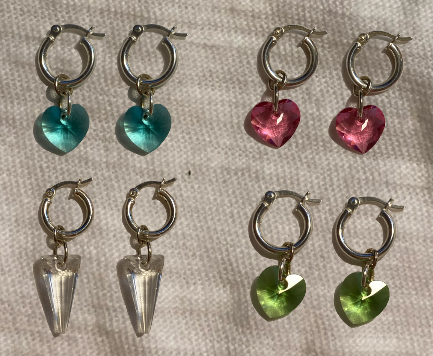 flat lay image from top left: blue crystal heart, pink crystal heart, clear crystal spike, and green crystal heart.